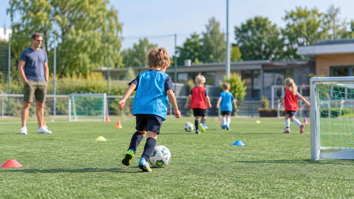 Ein Kind dribbelt auf einem kleinen Fußballfeld vor einem Vater
