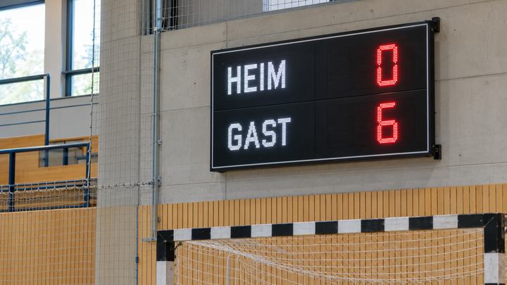 Nahaufnahme einer modernen Hallen-Anzeigetafel mit HEIM 0 und GAST 6; darunter ist der obere Teil eines Hallenfußballtors zu sehen.